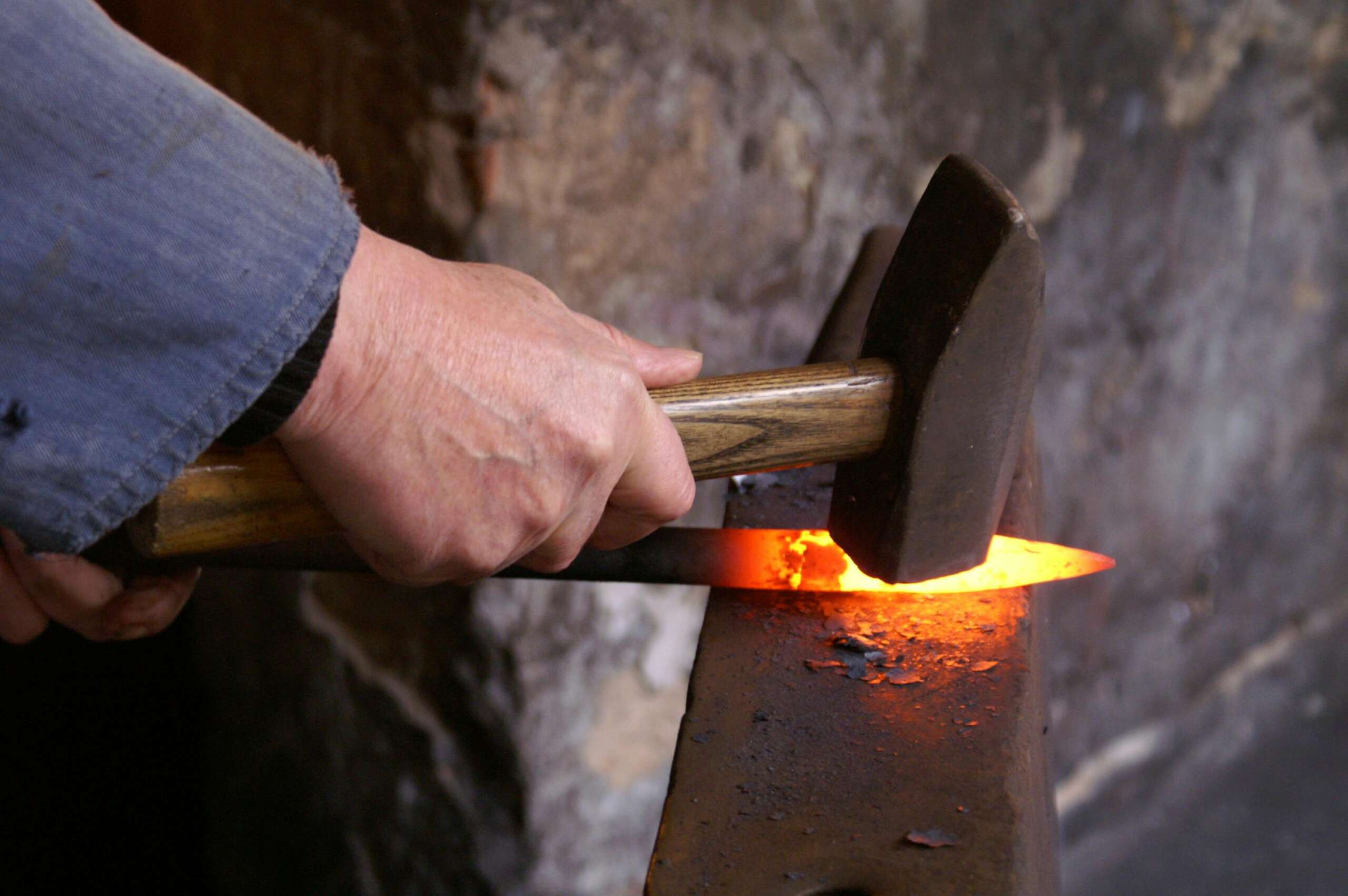 A blacksmith shaping glowing metal using a hammer on an anvil inside a forge.