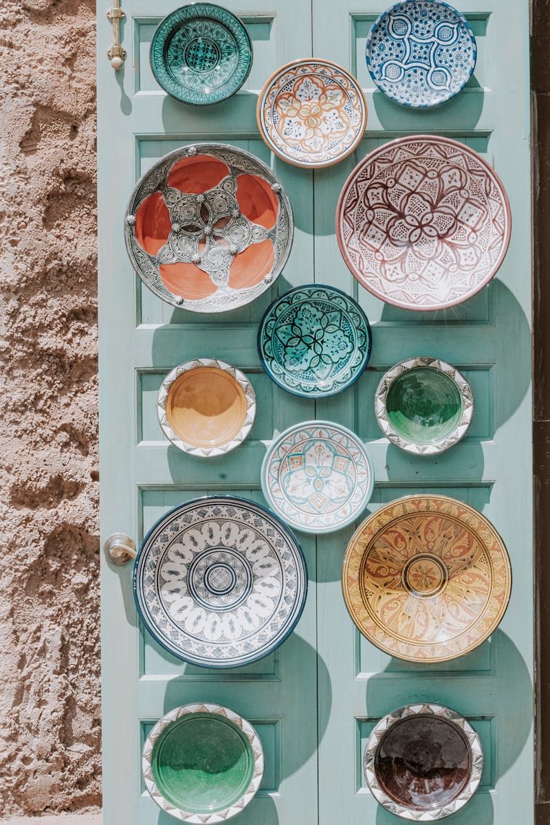 An artistic display of colorful ceramic plates on a vintage turquoise door outdoors.